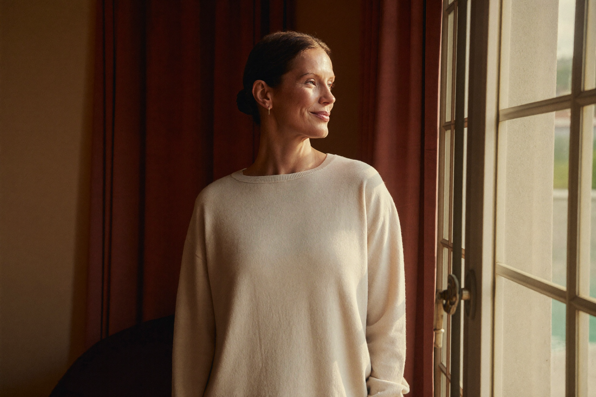 A poised woman at ease by a window in warm natural light, restored and unmistakably herself